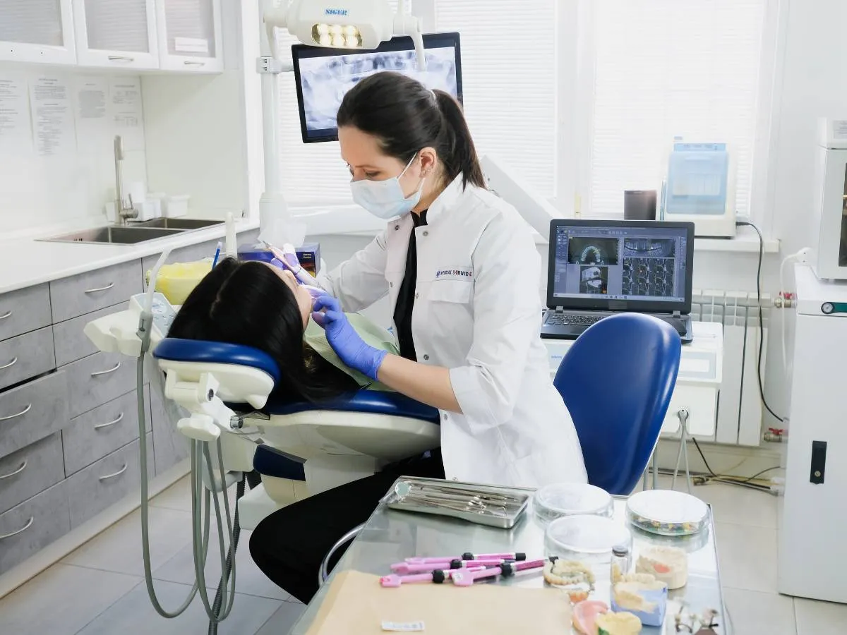 Dentista con mascarilla y guantes atiende a una paciente en el sillón