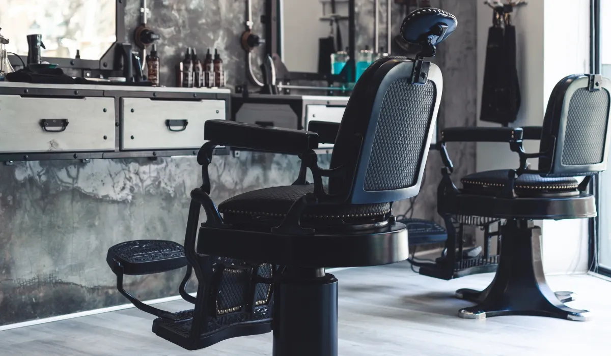 Dos sillones negros de barbero frente a un mostrador con productos