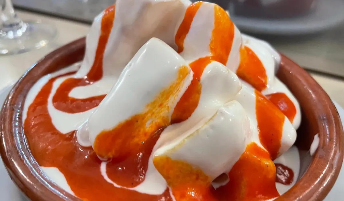 Patatas bravas con salsa blanca y salsa picante en una cazuela de barro