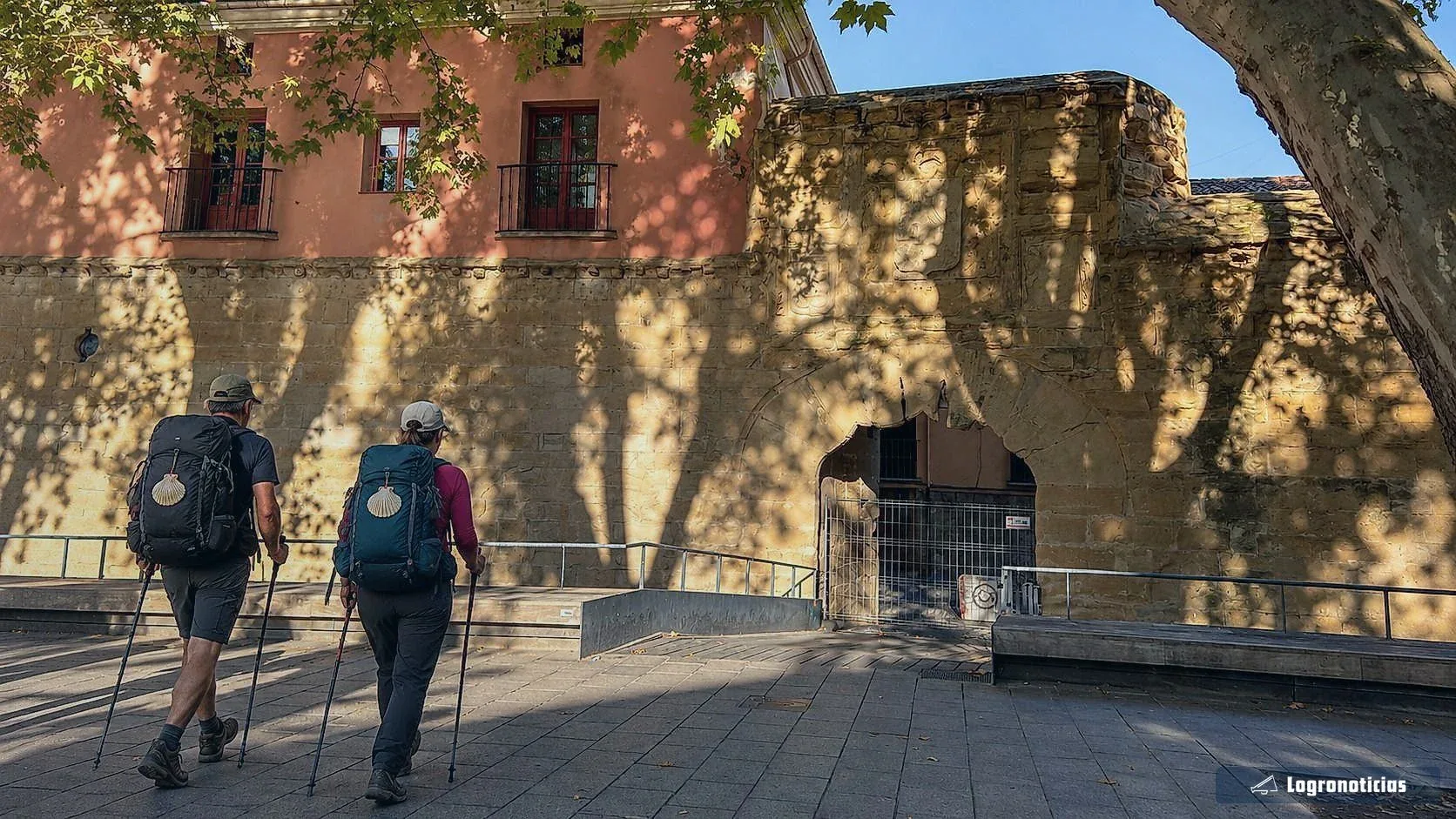 Peregrinos con mochila caminando junto a una muralla del casco antiguo por la mañana