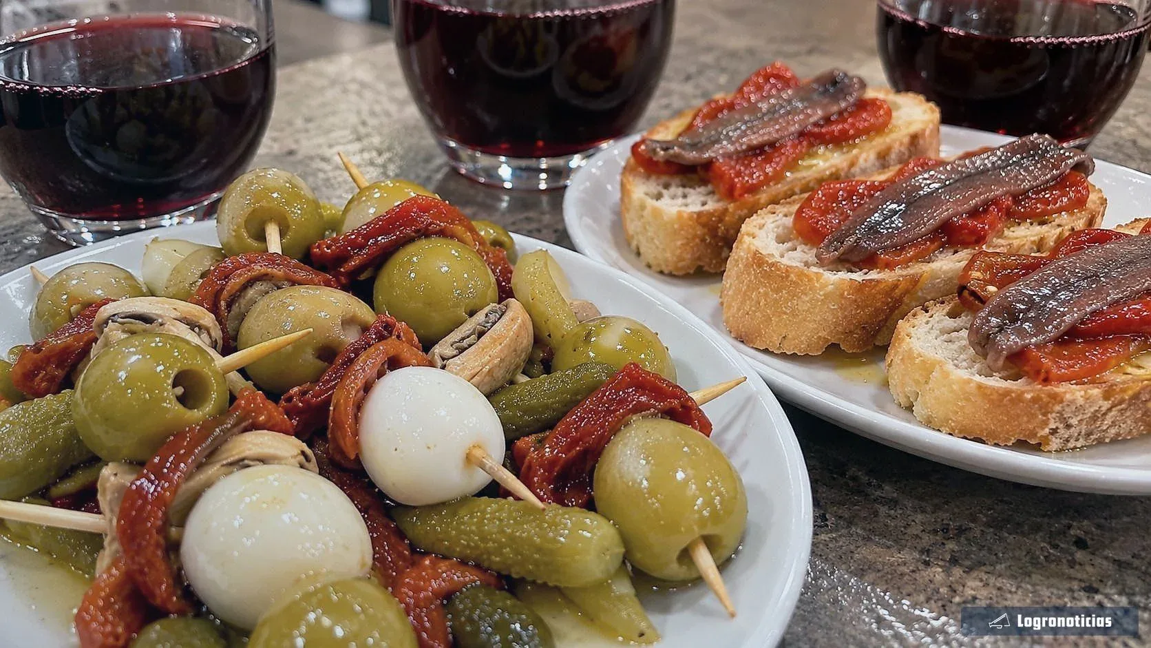 Vasos de vino tinto con banderillas de aceitunas y tostas de anchoa sobre una barra