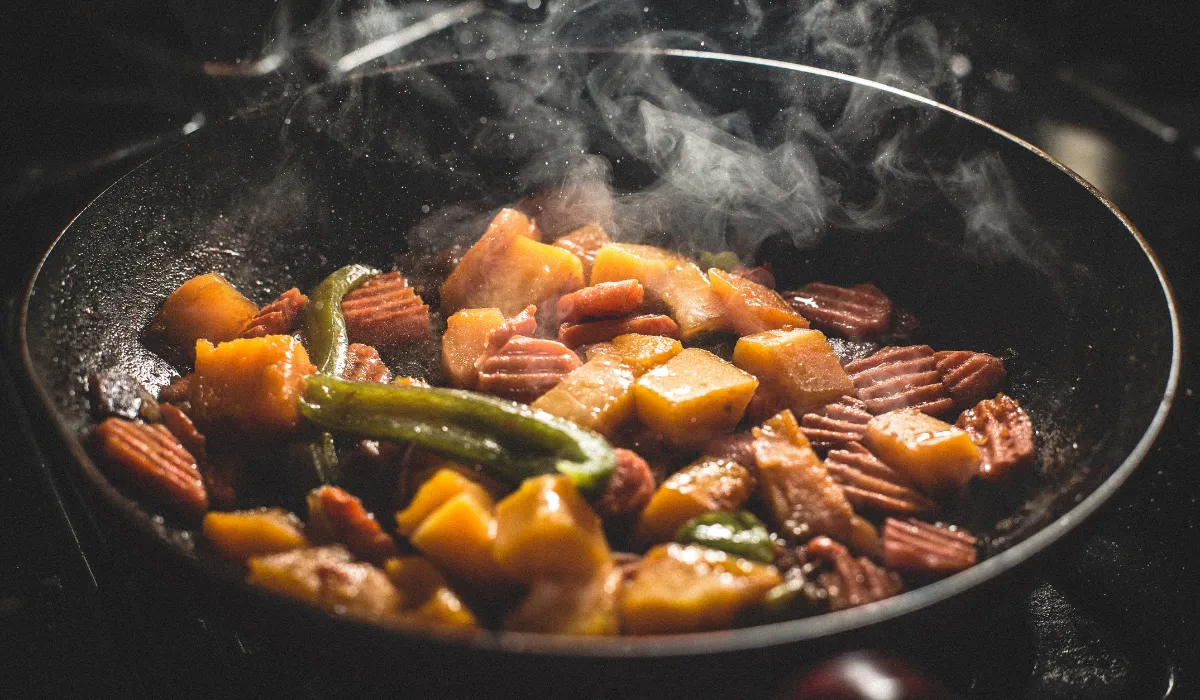 Sartén humeante con verduras y embutido troceado durante el salteado