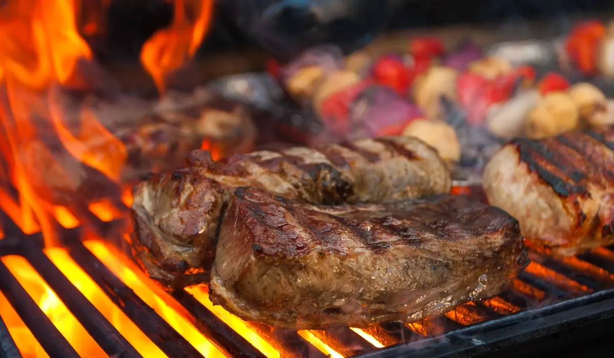 Piezas de carne dorándose sobre la parrilla con llamas a un lado
