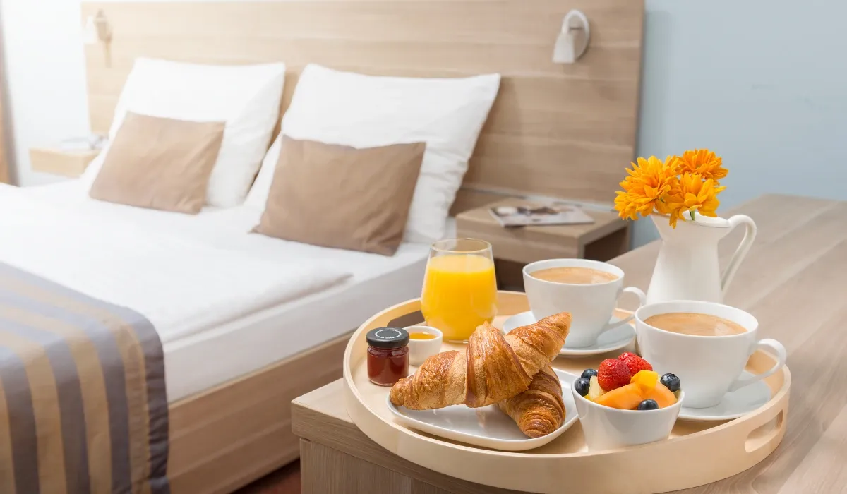 Bandeja de desayuno con cruasanes, café y zumo junto a la cama