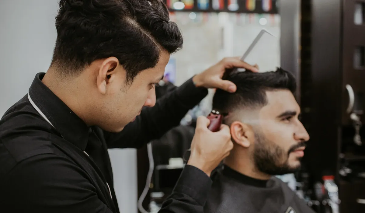 Barbero rebaja con máquina el lateral del pelo de un cliente