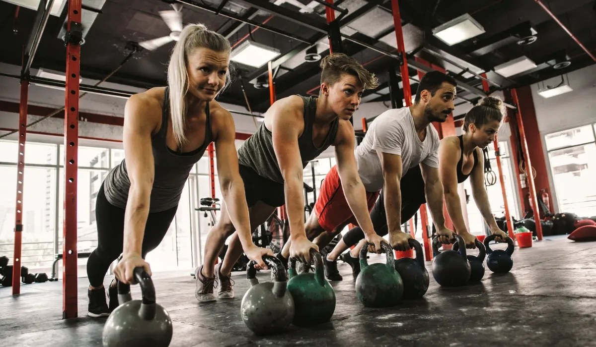 Cuatro deportistas hacen flexiones apoyados sobre pesas rusas en fila