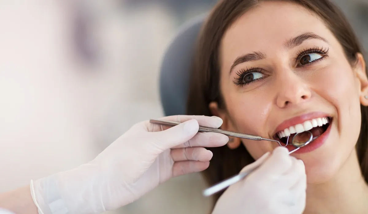 Paciente sonriente durante una revisión dental con espejo y sonda