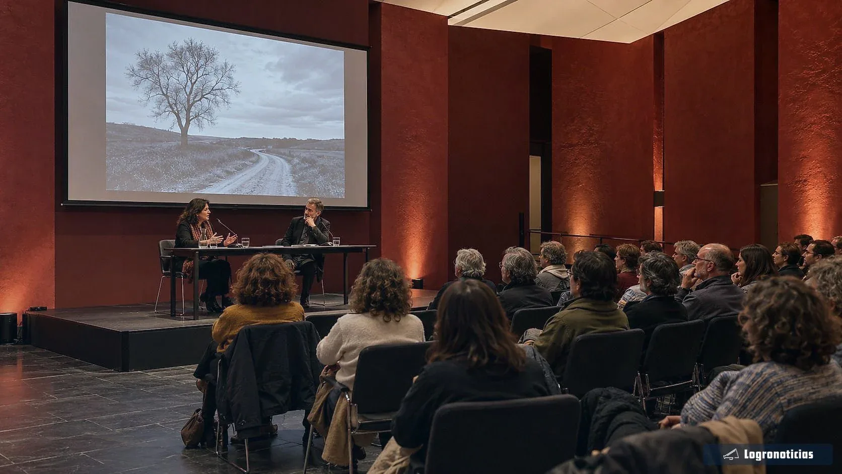 Público escuchando una conversación entre dos ponentes en una sala de actos