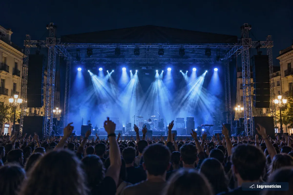 Escenario de un concierto nocturno con focos azules y público con los brazos en alto