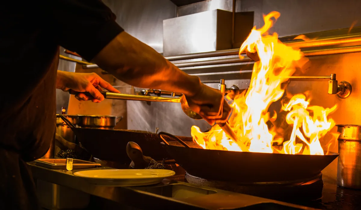 Cocinero saltea en un wok con una gran llamarada en una cocina profesional