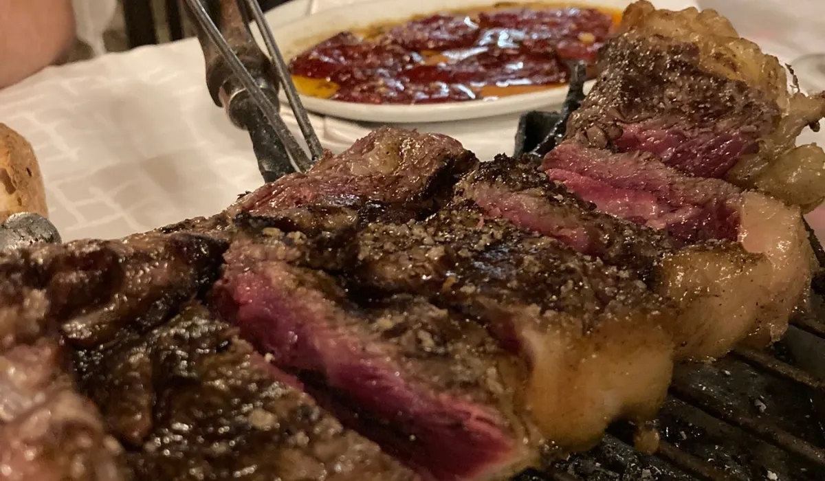Chuletón trinchado y poco hecho junto a una fuente de pimientos asados