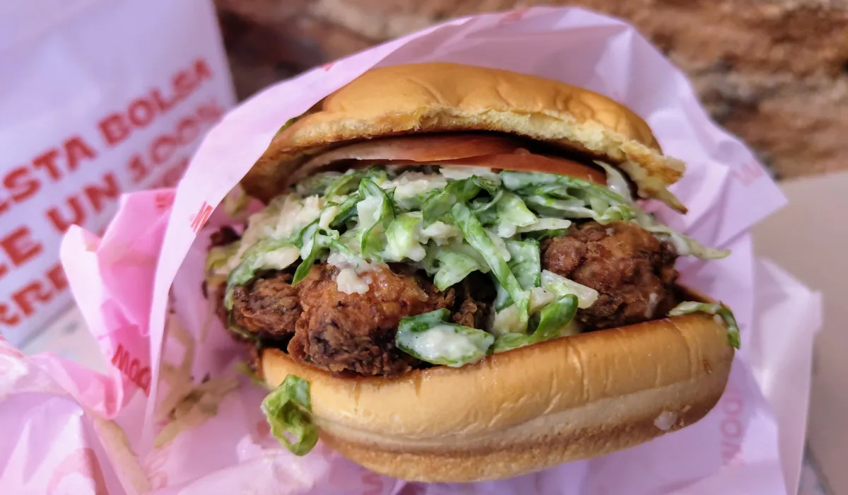 Hamburguesa de pollo crujiente con lechuga aliñada envuelta en papel rosa