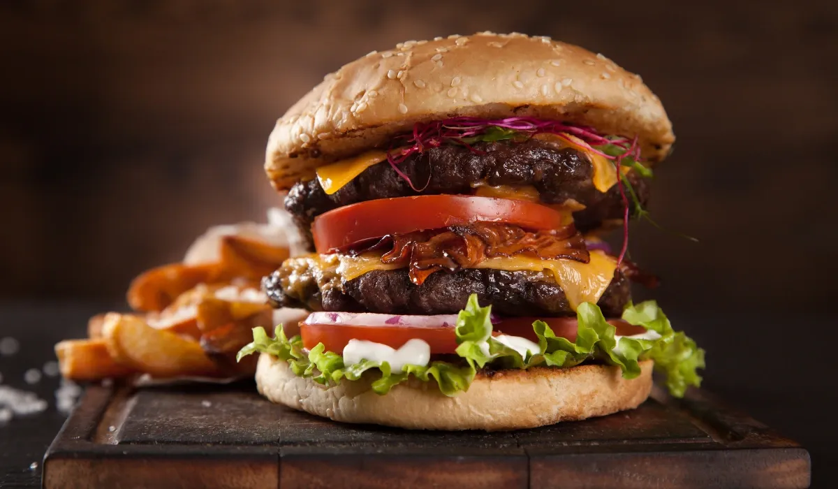 Hamburguesa doble con queso cheddar, beicon y tomate junto a patatas gajo