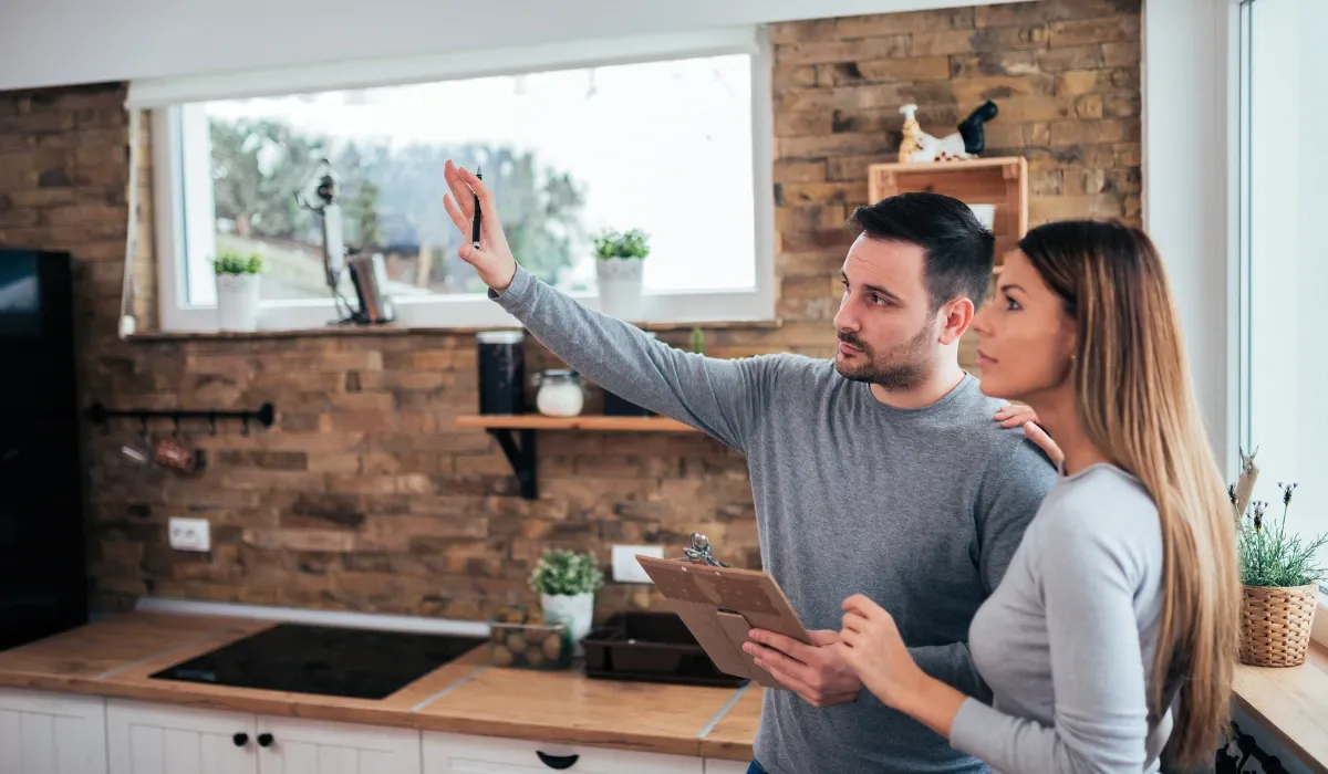 Pareja toma medidas y apunta ideas en una cocina con pared de ladrillo