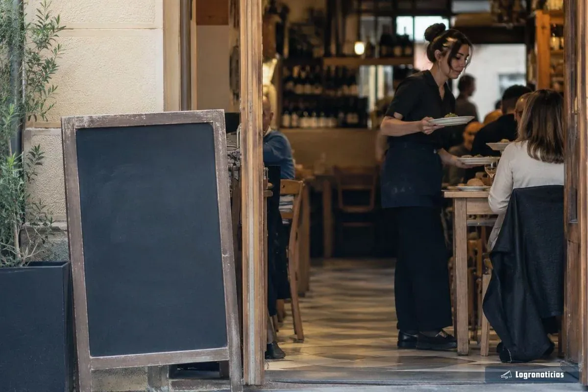 Puerta de un comedor a mediodía con pizarra y camarera sirviendo