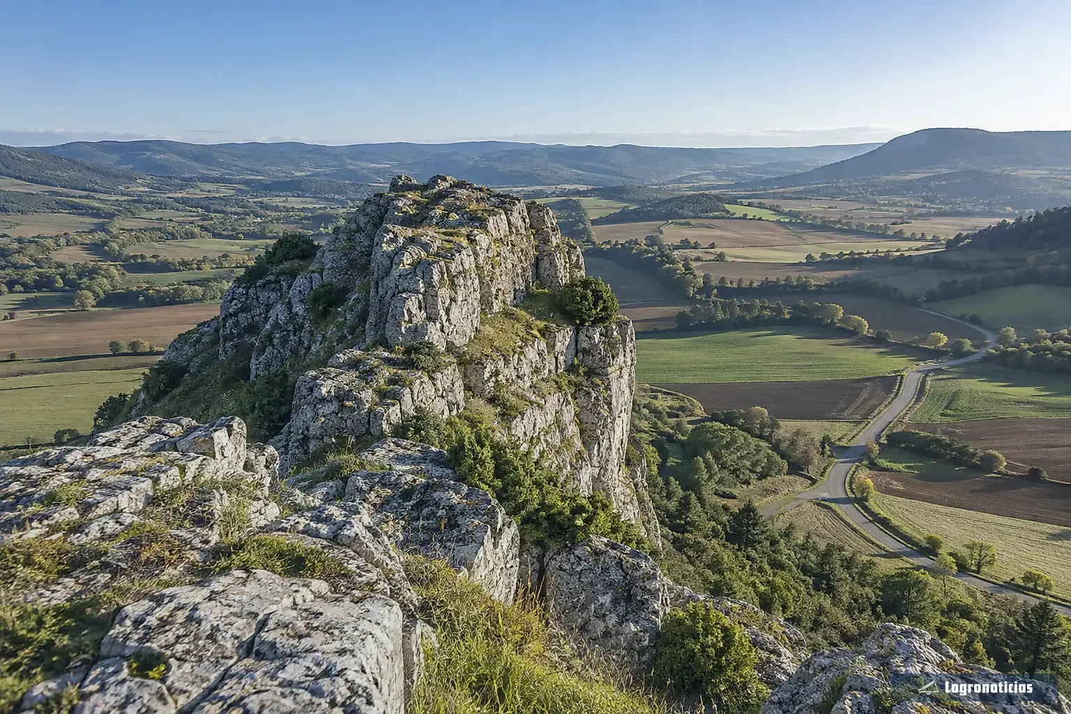Peñas rocosas sobre un valle con campos y una carretera al fondo