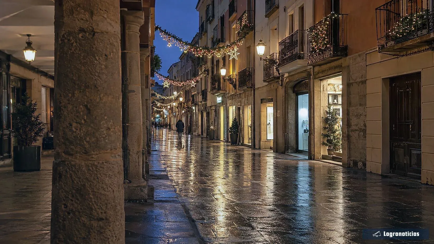 Calle peatonal con guirnaldas de luces y escaparates iluminados vista desde unos soportales