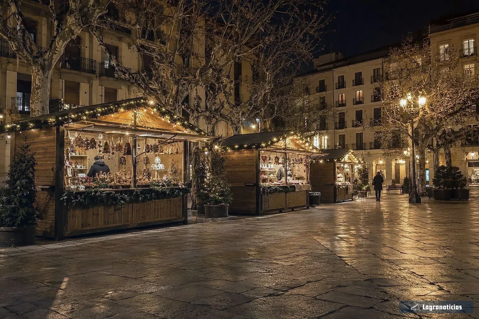 Puestos de madera de un mercado navideño iluminados en una plaza de noche