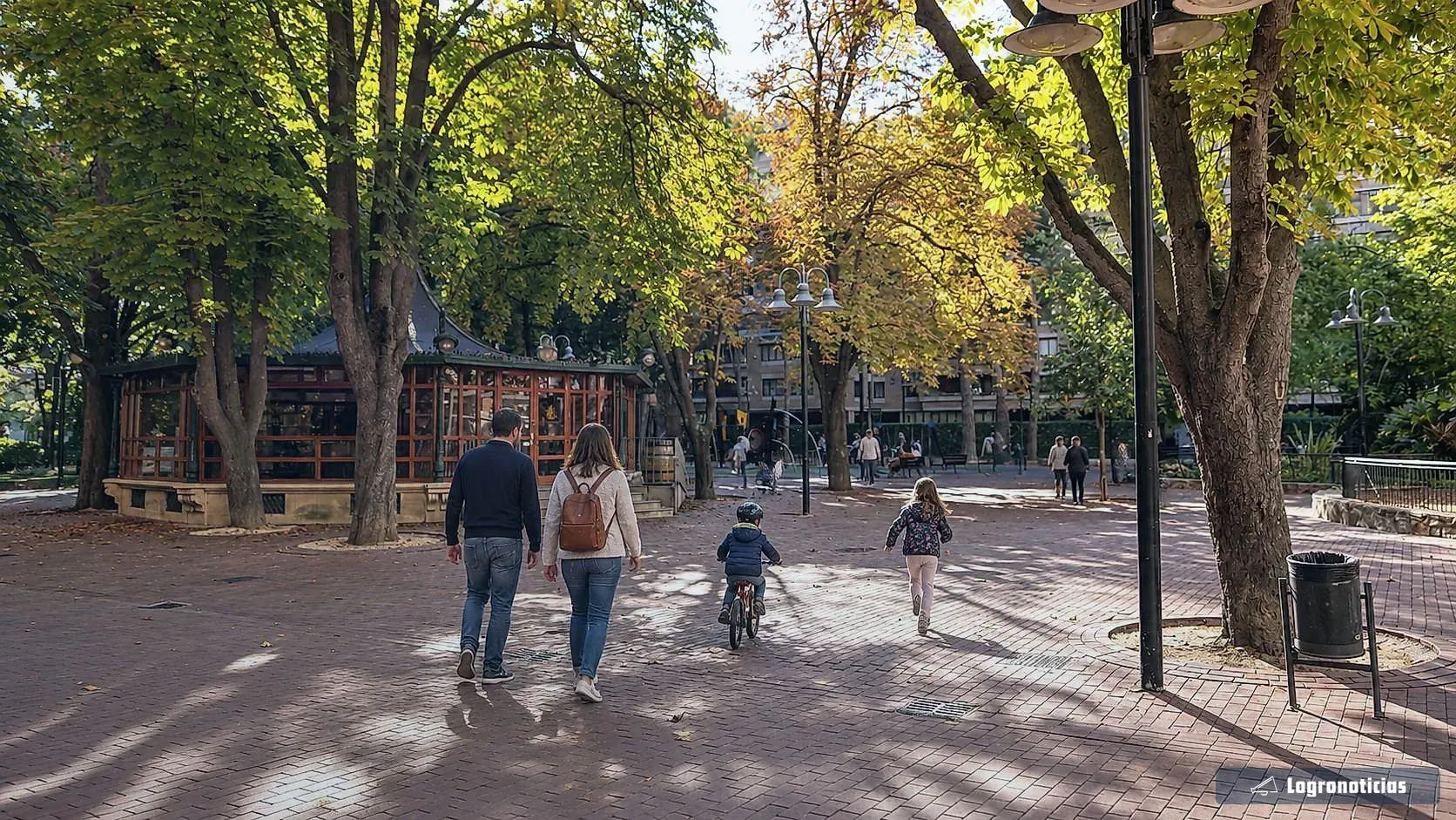 Familia con dos niños, uno en bicicleta, paseando por un parque en otoño