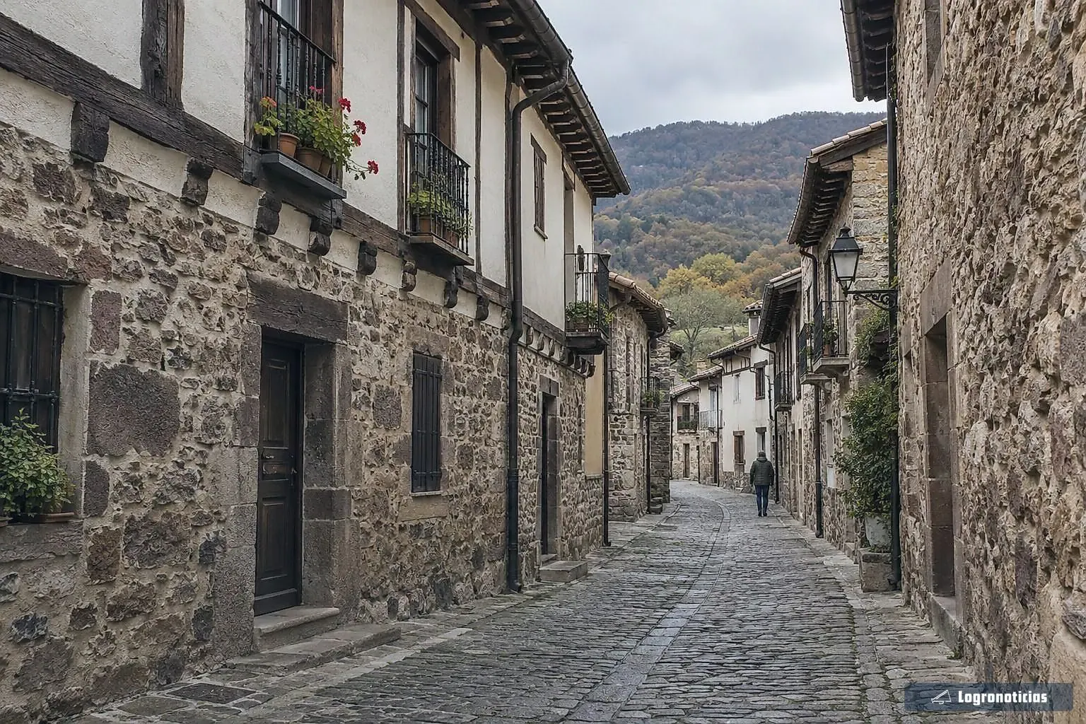 Calle empedrada de un pueblo con casas de piedra y balcones con flores