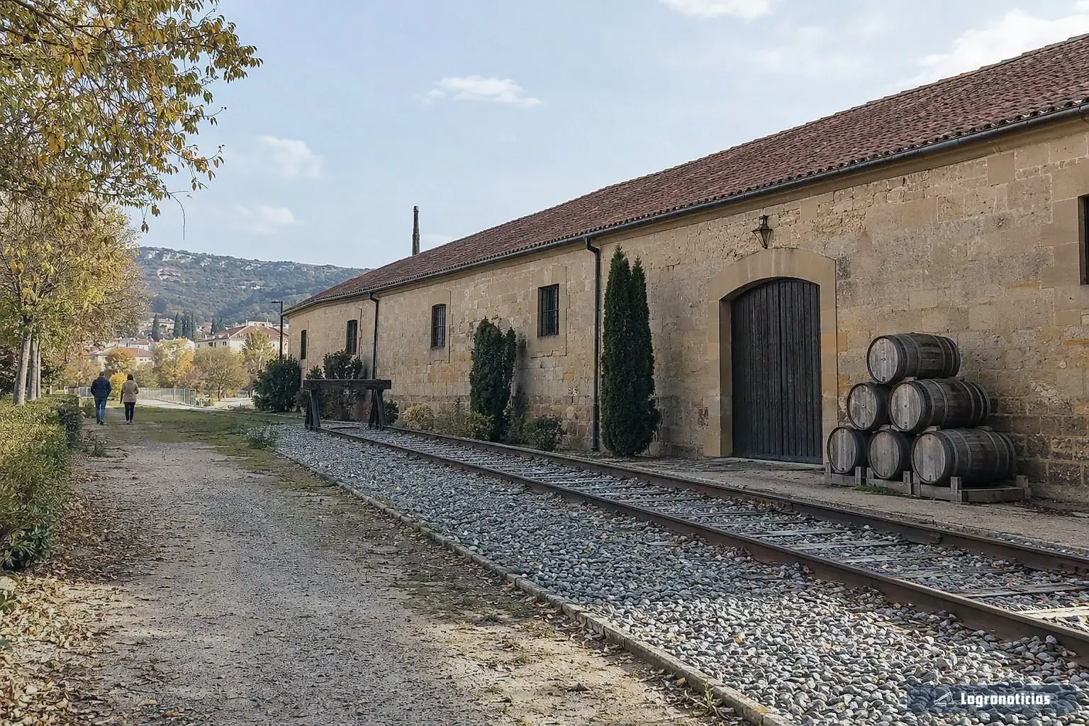 Bodega centenaria de piedra con barricas junto a una vía de tren