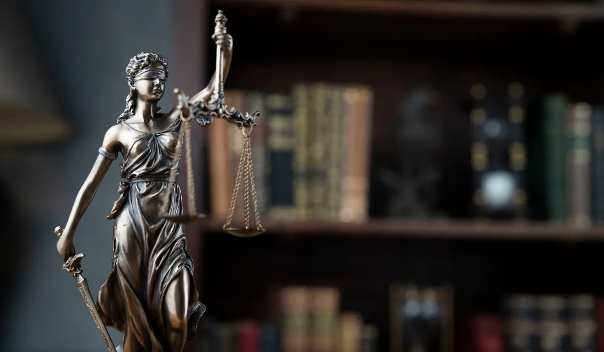 Figura de bronce de la justicia con balanza ante una estantería de libros