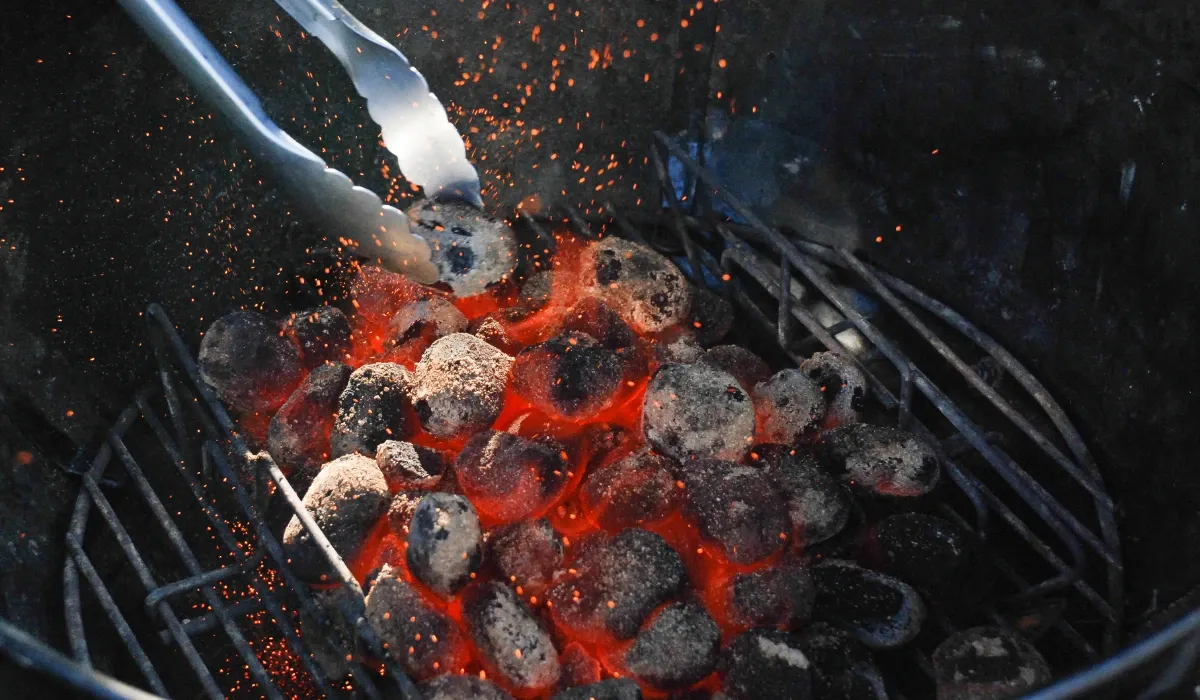 Pinzas metálicas colocando carbón al rojo vivo dentro de una barbacoa