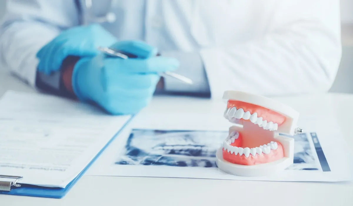 Modelo de dentadura sobre una radiografía junto a un dentista con guantes azules