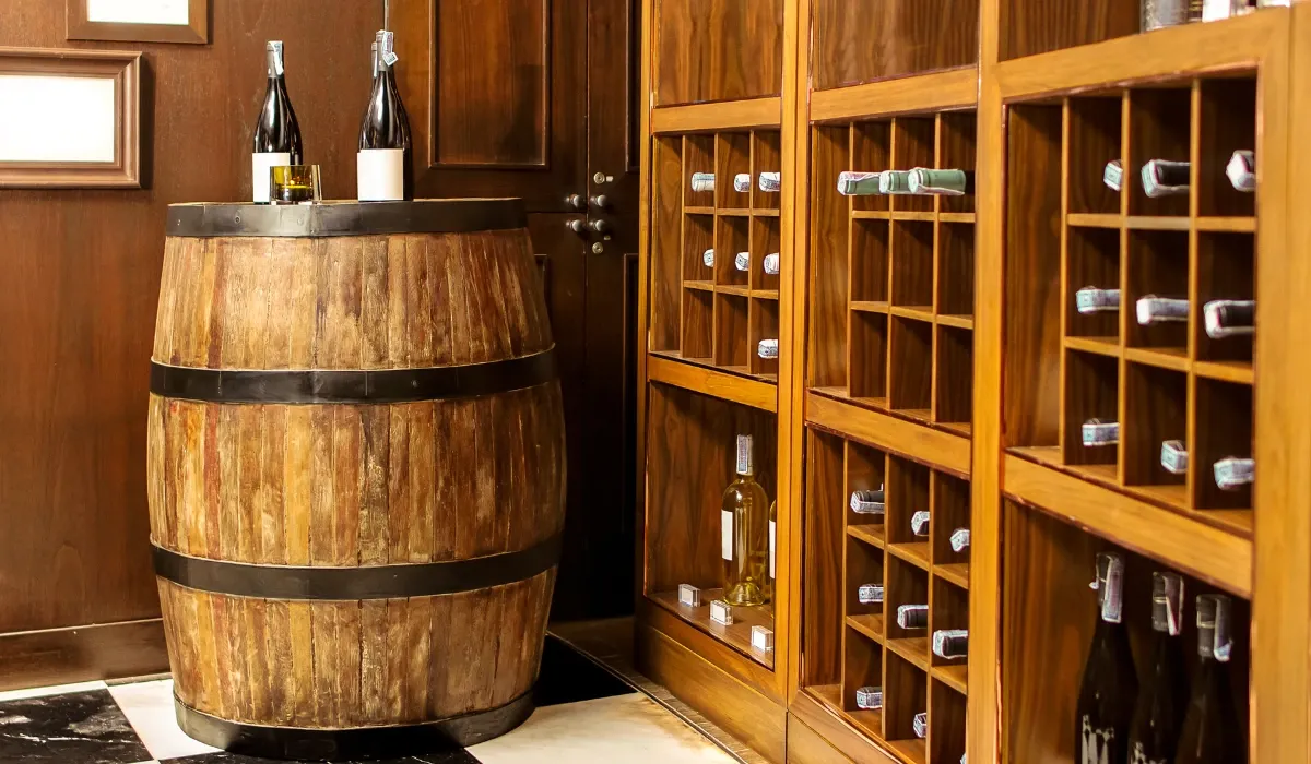 Barrica de madera con dos botellas junto a un botellero de pared